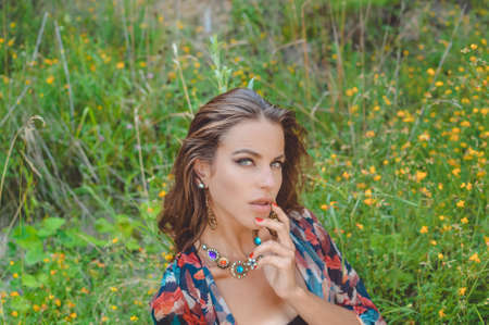 Closeup portrait of beautiful sensual young lady in fancy necklace sitting in wildflowers. Pretty...