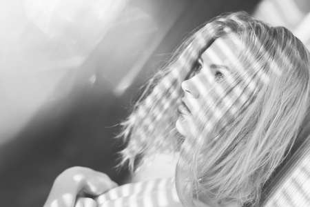 Close up on sensual beautiful young lady with shadow from window blinds on shoulders. Girl having fun looking at sun light flare rays on light copy space background. Black and white photographyの写真素材