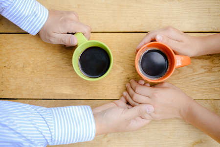 Picture closeup of hands and two coffee mugs. Top view of romantic conversation with tasty drinks on wooden table background.の写真素材