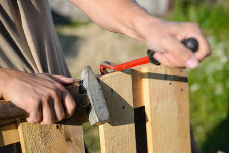 Picture of wood fence gate repairing. Closeup of male hands with crowbar and hammer on blurred...