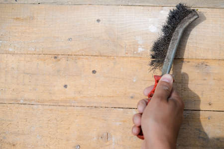 Picture of hand with aged metal brush. Closeup of scrubbing and cleaning on wooden plank surface background.の写真素材