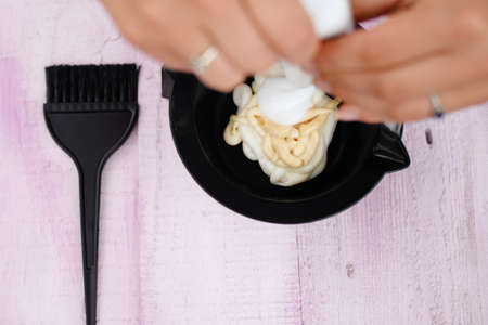 Picture of woman's hands mixing dyes for hair in black bowl. Closeup of hairdresser's equipment on...