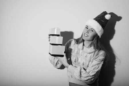 Portrait of exciting pretty girl in Santa hat with gifts. Black and white photography