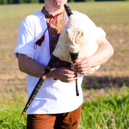 Picture of man enjoying playing pipes in Ukrainian traditional shirt on green outdoors copy space summer field backgroundの写真素材