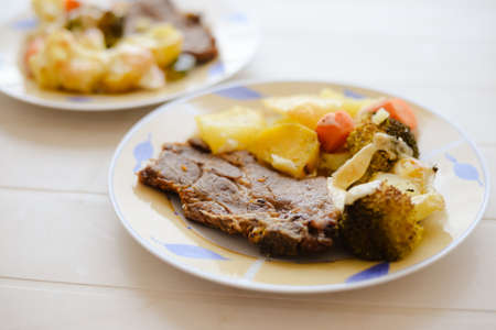 Picture of plates with beautiful pork steak and sweet potatoes standing on table. Tasty traditional dish on blurred bright table background.の写真素材
