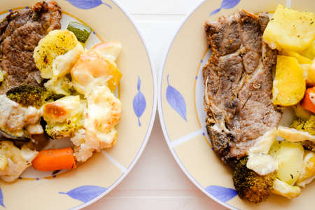 Picture of two plates with beautiful pork steak and baked vegetables. Tasty traditional dish on blurred bright table background.の写真素材