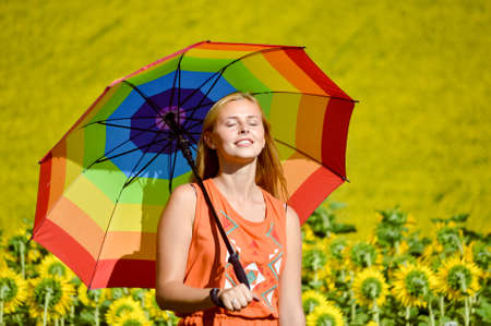 Portrait of beautiful young woman holding rainbow umbrella on the sunflower field outdoors backgroundの写真素材