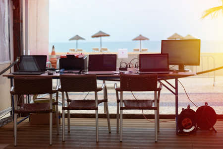 Picture of openair office place beside tropical beach. Laptops and monitor on desk on sunny seaside blurred background.の写真素材
