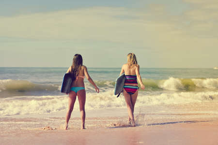 Picture of beautiful young women walking away with surfboards. Back view of pretty girls on blurred seascape background.の写真素材