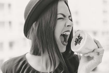 Side view monochrome portrait of young female in hat opening mouth wanting to bite ripe papaya fruitの写真素材