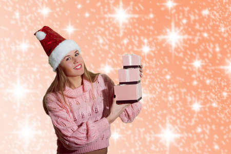 Portrait of beautiful exciting young lady in Santa Claus red hat holding gift boxes on abstract festive design background and happy smileの写真素材
