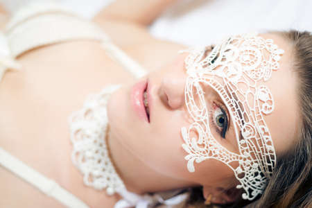 Closeup portrait of lovely beautiful girl in white bustier wearing lace mask on light backgroundの写真素材