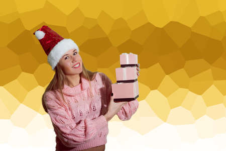 Portrait of beautiful exciting young lady in Santa red hat holding gift boxes on abstract festive design background and happy smileの写真素材