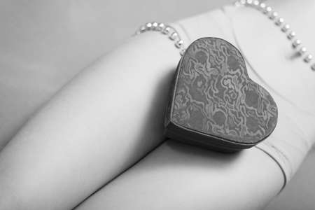 Closeup picture on present gift box in the form of heart lying on beautiful sexy female legs. Black and white photographyの写真素材