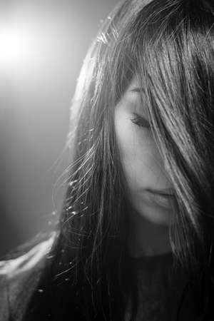 Closeup black and white photography of dreaming beautiful girl holding eyes closed posing on light flare copy space backgroundの写真素材