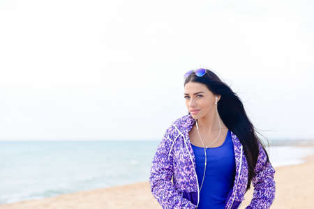 Portrait of sport pretty woman listening music on the beach backgroundの写真素材