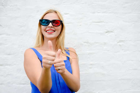 Beautiful blond girl happy pointing fingers thumbs up watching movie with 3D glasses, exciting screaming. Closeup portraitの写真素材