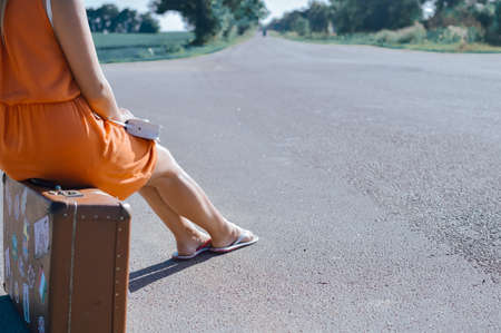 Back side view of young pretty woman hitchhiking waiting along the road for a ride on sunny outside summer backgroundの写真素材