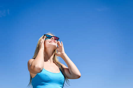 Beautiful young lady watching movie with 3D glasses, holding hands up in excitement on light blue background. Closeup portraitの写真素材
