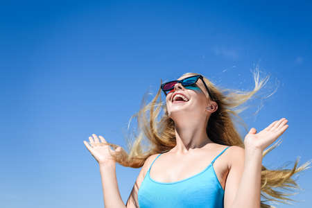 Beautiful young lady watching movie with 3D glasses, exciting holding hands up on light blue...