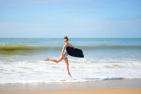 Joyful surfer girl happy cheerful running surfing at ocean beach water. Female bikini heading for...