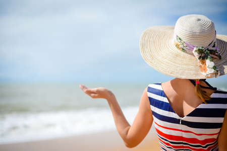 Back view of elegant woman holding hand palm up with sea on the background, summer vacation concept