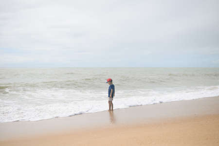 Back view of little boy walking along the beach during the sunset outsideの写真素材
