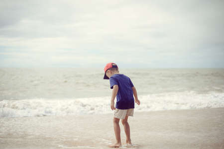 Back view of little boy walking along the beach during the sunset outsideの写真素材
