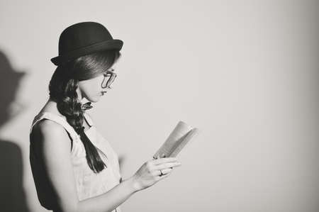 Black and white picture of beautiful girl reading a book against light wall background, portrait