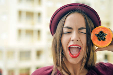 Portrait of amazing exciting beautiful elegant female wearing red felt hat holding half of papaya...