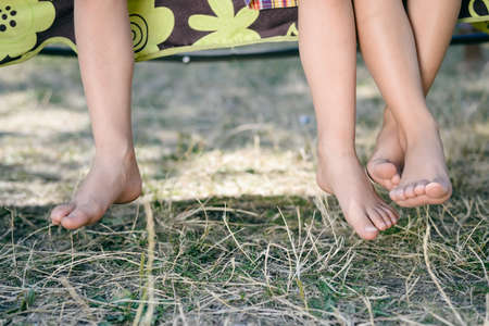 Outdoor picture of two children legs barefoot. Closeup of happy kids sitting on sunny countryside background.の写真素材