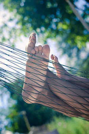 Closeup of happy family lying on hammock on sunny countryside background. Picture of man and children legs barefoot.の写真素材