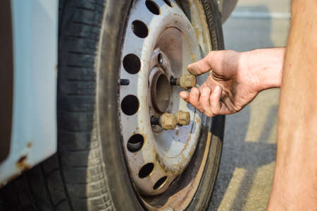 Closeup of person checking fixing bolts on vehicle tire with bare hands. outdoors photoの写真素材