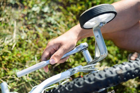Closeup on hands of male fixing mechanism of the bicycle, green outside background