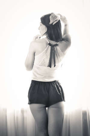 Back side view of sensual beautiful female over the window background. Sexy female looking outの写真素材