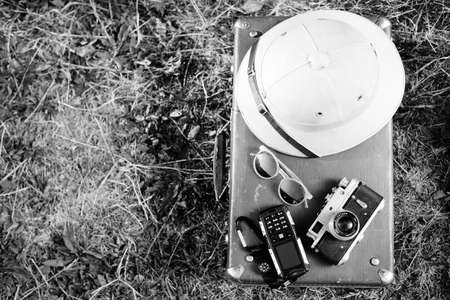 Black white photography top view pithhelmet, old camera, cellphone and sunglasses on retro suitcase,...