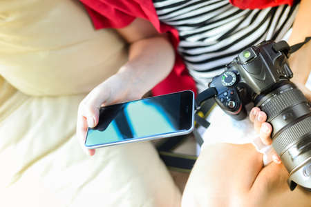 Person working with DSLR camera and smartphone, light background. Close up top view mockup screen