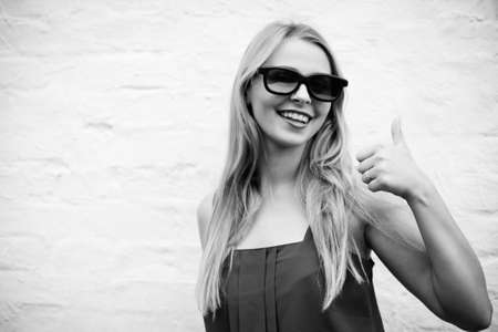 Black and white picture of joyful blond girl in 3d glasses happy smiling. Young woman showing thumb up on light wall background.の写真素材