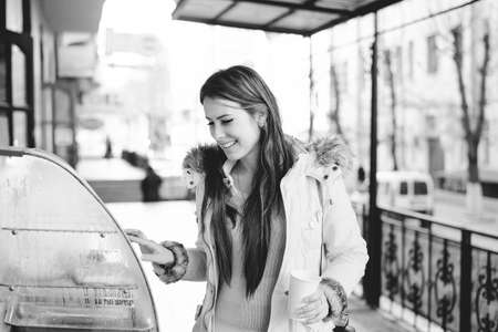 Black and white photography of tourist woman with long hair looking at the shop display. Smiling lady posing with with a cup of coffee in her hand, outdoors backgroundの写真素材