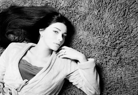 Black and white picture of beautiful young woman laying on fluffy soft carpet indoor backgroundの写真素材