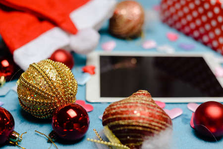 Festive blurry background with white blank tablet mobile computer display and Christmas toys. Mock...