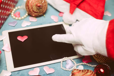 Festive background with Santa hand using white blank tablet mobile computer display and Christmas...