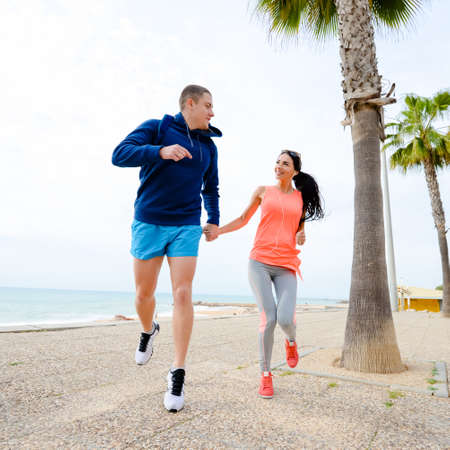 Portrait of happy young couple running together, ocean beach embankment outdoors background