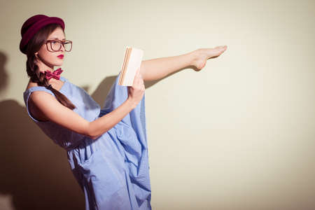 Elegant pretty girl in a red hat and glasses reading a book on light background