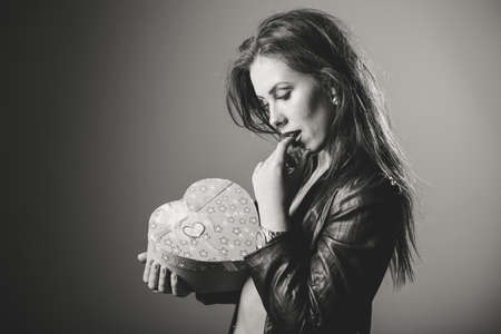 Happy beautiful stylish glamor woman in black leather jacket holding love heart shapped gift box, studio shot on light background. Valentine dayの写真素材
