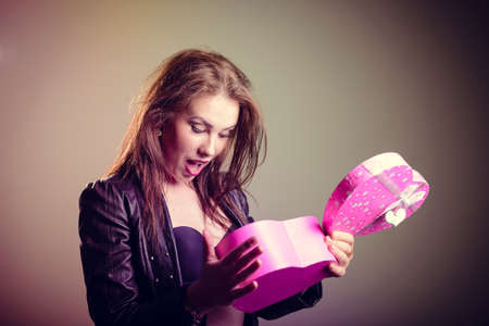 Happy beautiful stylish glamor woman in black leather jacket holding love heart shapped gift box, studio shot on light background. Valentine dayの写真素材