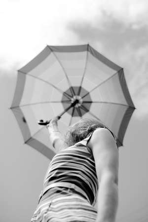 Black and white photography of elegant female under umbrella looking up in cloud sky. Woman in striped dress rising parasol.の写真素材