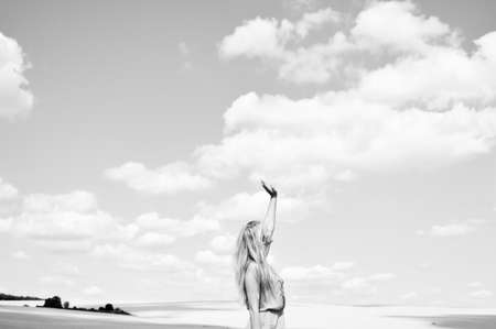 Black and white photography of female lifting arm standing in field over cloudy sky background. Concept of faithの写真素材