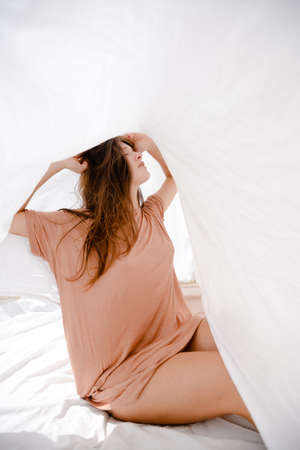 Hiding woman playing with a bed sheet over light copy space backgroundの写真素材