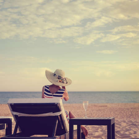 Woman on a tropical beach holiday. Luxury wooden lounge and sunny outdoors backgroundの写真素材